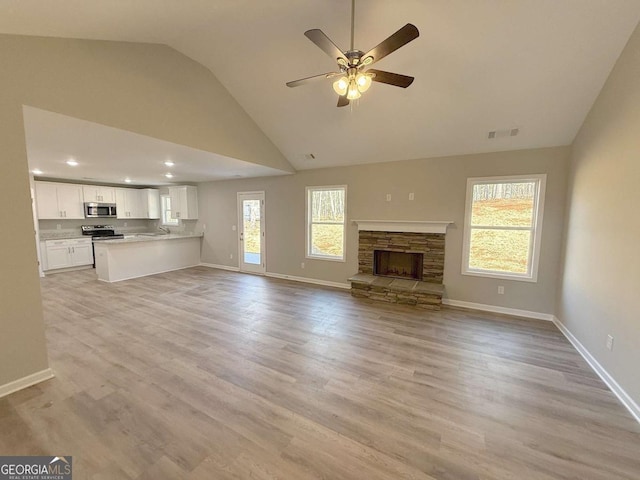 unfurnished living room featuring a stone fireplace, ceiling fan, light hardwood / wood-style flooring, and a healthy amount of sunlight