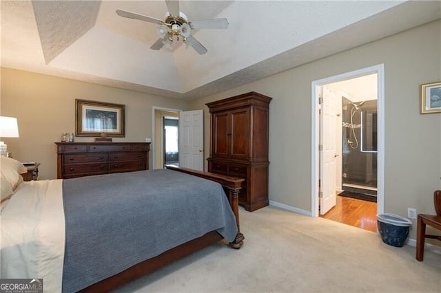 carpeted bedroom featuring connected bathroom, a raised ceiling, and ceiling fan