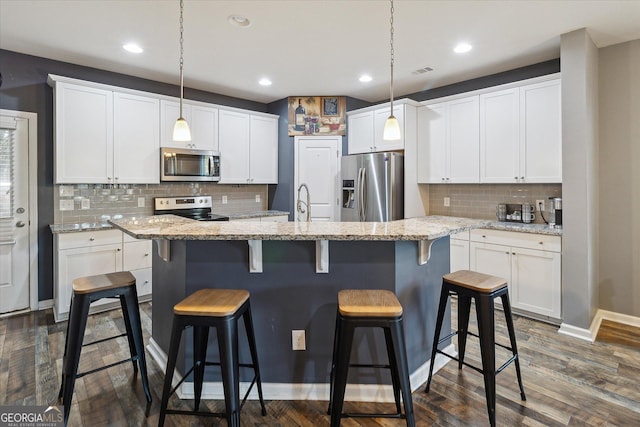 kitchen featuring white cabinets, pendant lighting, stainless steel appliances, and an island with sink