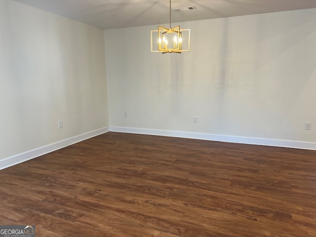 empty room featuring dark wood-type flooring and an inviting chandelier