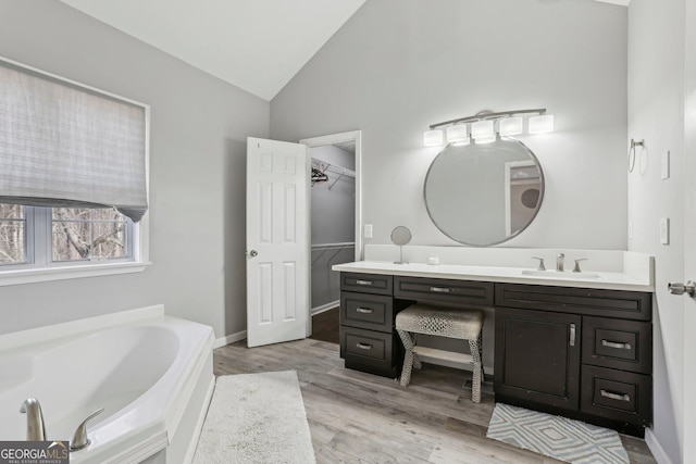 bathroom featuring hardwood / wood-style flooring, vanity, lofted ceiling, and a bath