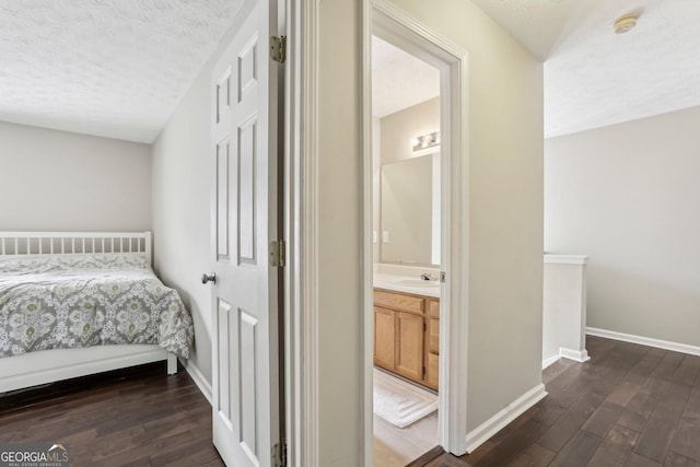 bedroom with a textured ceiling, connected bathroom, dark hardwood / wood-style floors, and sink