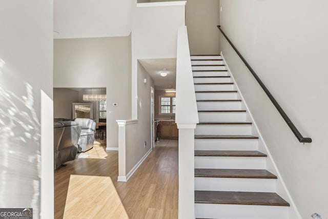 stairs with hardwood / wood-style flooring, a towering ceiling, and a chandelier