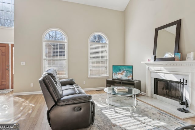 living room with a high end fireplace, a high ceiling, and light wood-type flooring