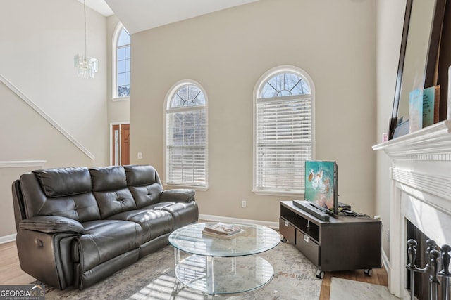 living room with light wood-type flooring, a high ceiling, a high end fireplace, and a chandelier