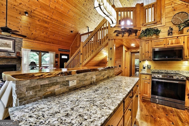 kitchen featuring wooden walls, light stone counters, decorative light fixtures, and appliances with stainless steel finishes