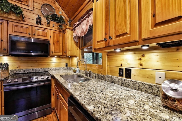 kitchen with wood walls, light stone countertops, sink, and appliances with stainless steel finishes