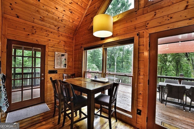 dining space featuring wood-type flooring, wooden ceiling, high vaulted ceiling, and wooden walls