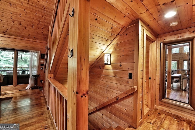 corridor with wood walls, hardwood / wood-style floors, wood ceiling, and lofted ceiling