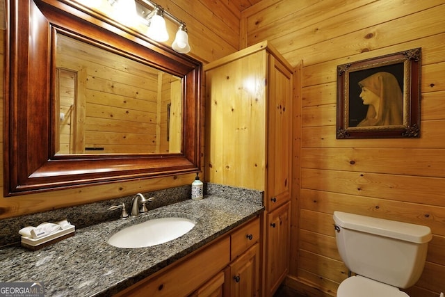 bathroom with vanity, wood walls, and toilet