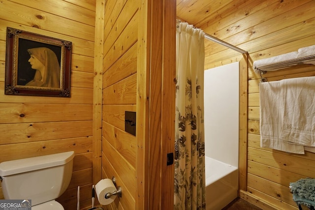 bathroom featuring toilet, shower / bath combo with shower curtain, and wooden walls