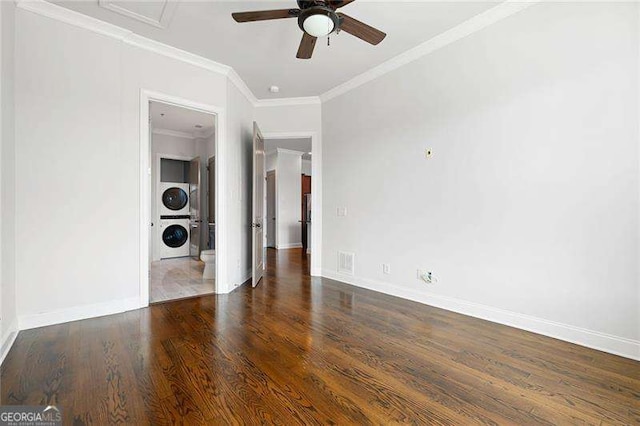 empty room featuring ceiling fan, dark hardwood / wood-style flooring, stacked washer and clothes dryer, and ornamental molding