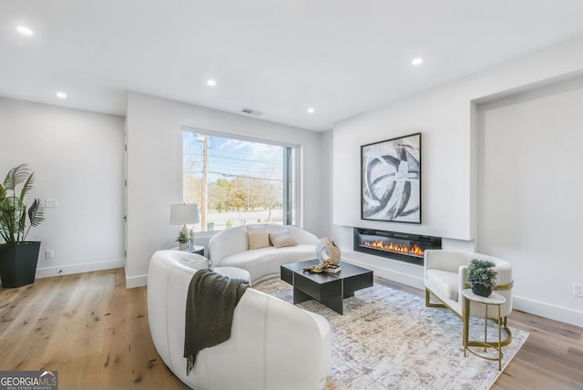 living area featuring recessed lighting, visible vents, baseboards, light wood finished floors, and a glass covered fireplace