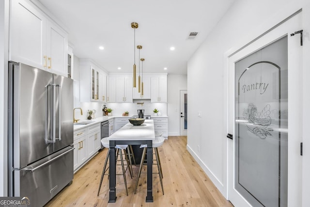 kitchen with white cabinets, glass insert cabinets, appliances with stainless steel finishes, hanging light fixtures, and light countertops