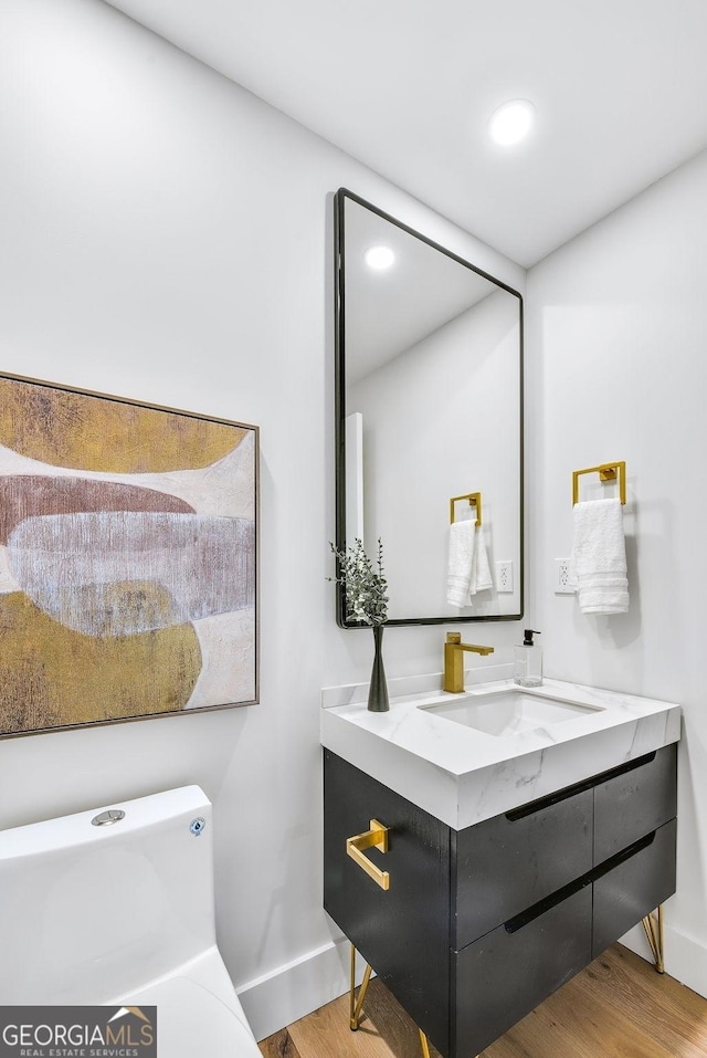 bathroom with toilet, recessed lighting, wood finished floors, vanity, and baseboards