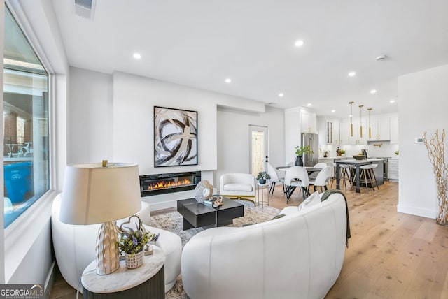 living area with visible vents, baseboards, a glass covered fireplace, light wood-style flooring, and recessed lighting