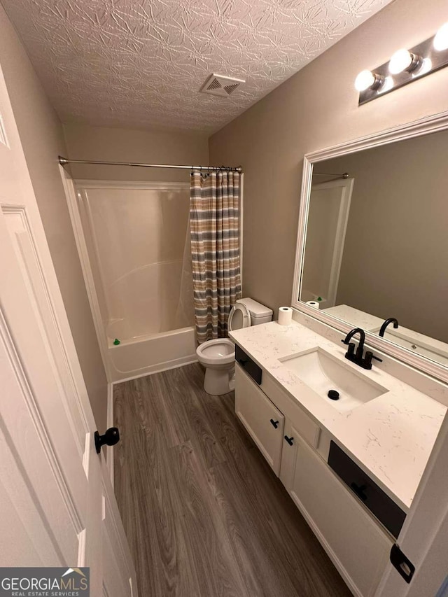 full bathroom with hardwood / wood-style floors, vanity, toilet, a textured ceiling, and shower / tub combo