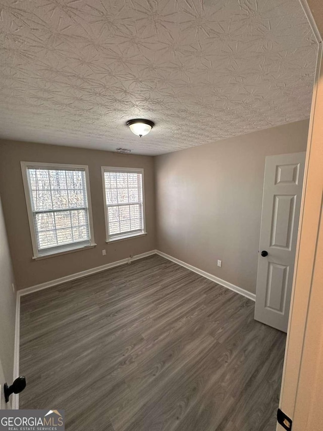 spare room featuring a textured ceiling and dark hardwood / wood-style floors