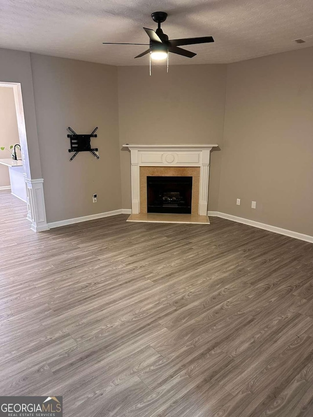 unfurnished living room featuring ceiling fan, wood-type flooring, a textured ceiling, and a high end fireplace