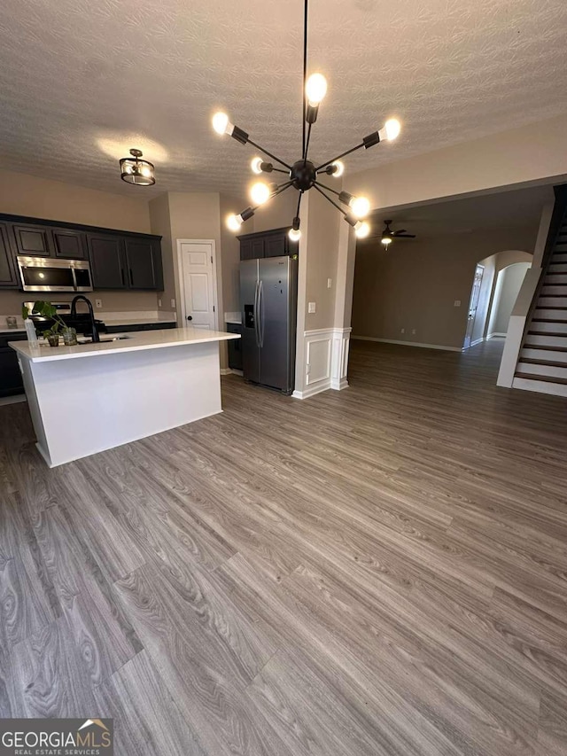 kitchen with sink, stainless steel appliances, dark hardwood / wood-style floors, a textured ceiling, and a kitchen island with sink