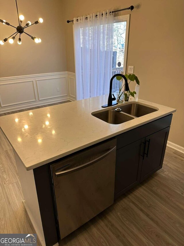 kitchen with light stone countertops, dishwasher, sink, an island with sink, and wood-type flooring