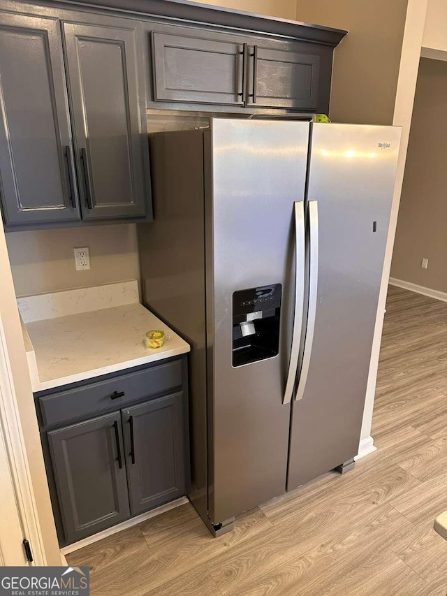 kitchen featuring stainless steel fridge, light stone countertops, and light hardwood / wood-style flooring