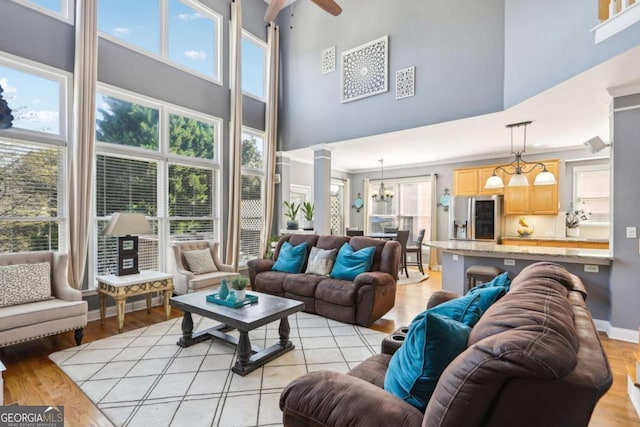 living room featuring ceiling fan with notable chandelier, a towering ceiling, decorative columns, and light hardwood / wood-style flooring