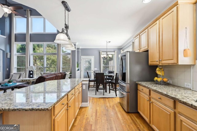 kitchen featuring a center island, ceiling fan with notable chandelier, hanging light fixtures, light hardwood / wood-style flooring, and tasteful backsplash