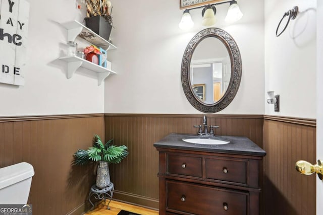 bathroom featuring wooden walls, vanity, and toilet