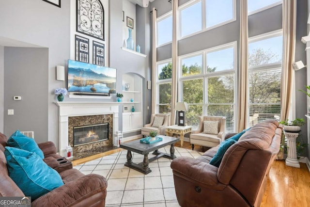 tiled living room with a high end fireplace, built in shelves, and a high ceiling