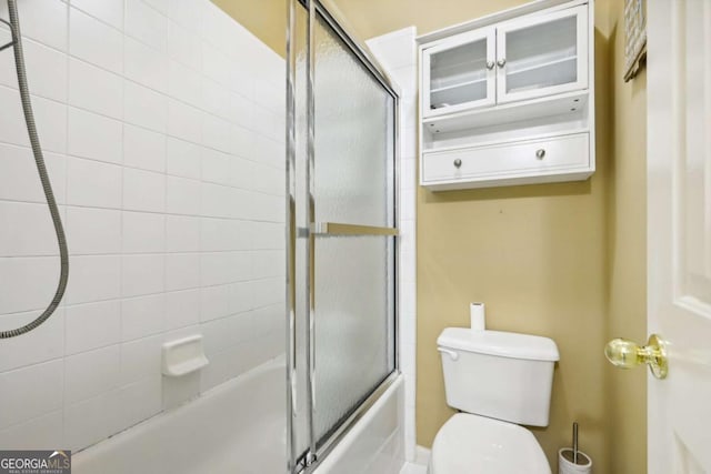 bathroom featuring toilet and bath / shower combo with glass door