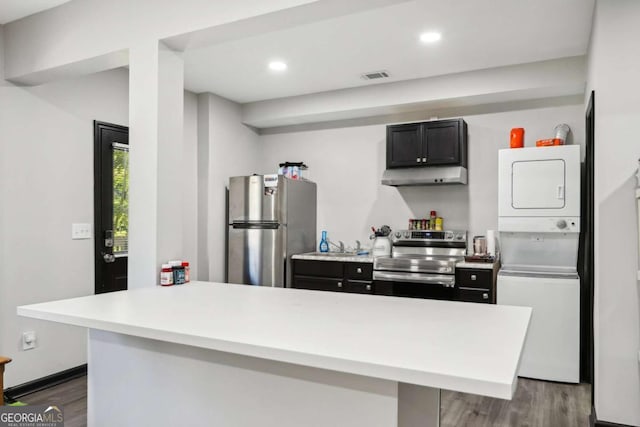 kitchen with kitchen peninsula, dark hardwood / wood-style flooring, stacked washer and dryer, and appliances with stainless steel finishes