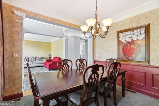 carpeted dining room featuring ornate columns, a notable chandelier, and crown molding