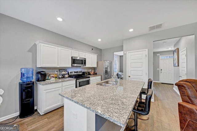 kitchen featuring a breakfast bar, a kitchen island with sink, white cabinets, sink, and appliances with stainless steel finishes