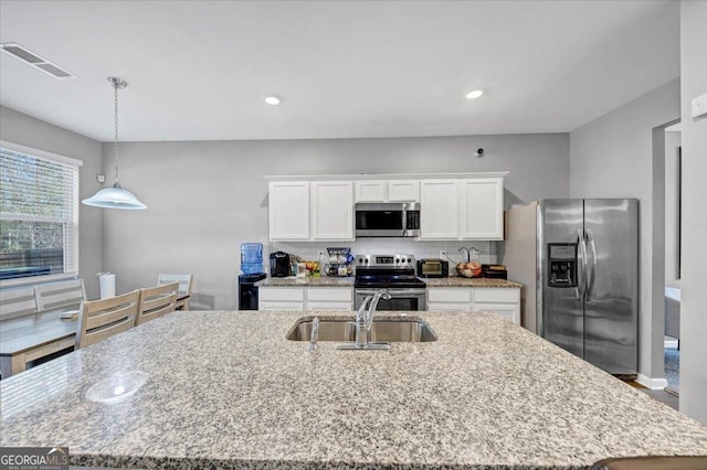 kitchen with sink, stainless steel appliances, an island with sink, decorative light fixtures, and white cabinets