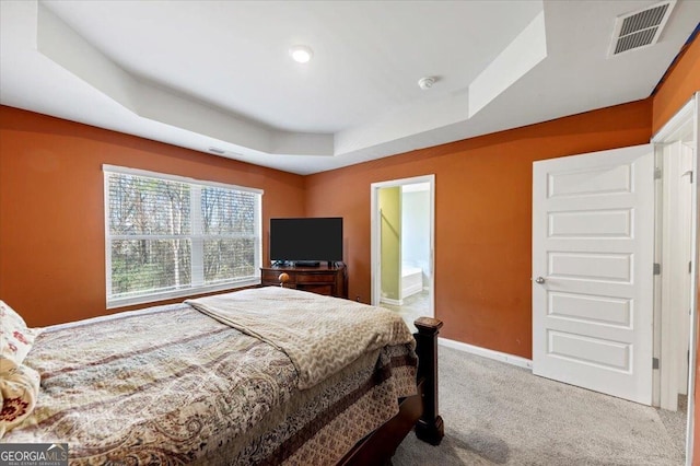 bedroom with carpet flooring, a raised ceiling, and ensuite bath