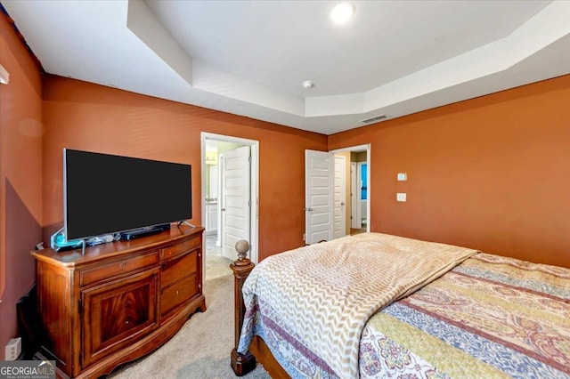 carpeted bedroom featuring a tray ceiling and ensuite bath