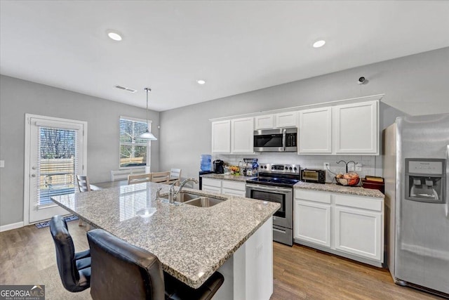 kitchen featuring stainless steel appliances, a kitchen island with sink, sink, decorative light fixtures, and white cabinetry