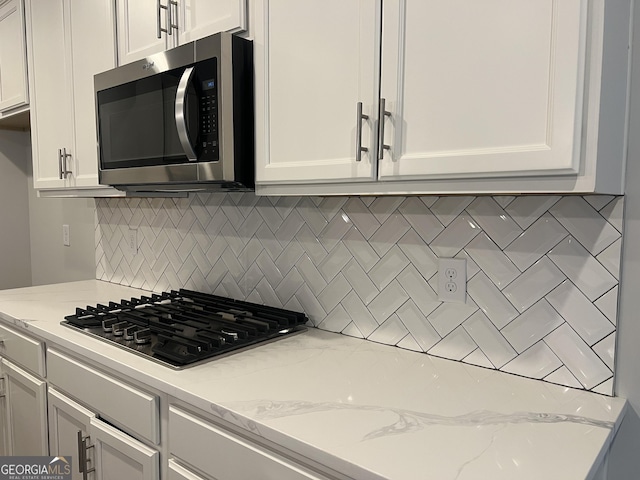 kitchen featuring light stone counters, white cabinetry, black gas stovetop, and tasteful backsplash