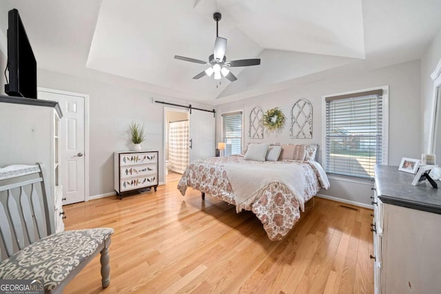 bedroom featuring a barn door, ceiling fan, light hardwood / wood-style floors, and lofted ceiling