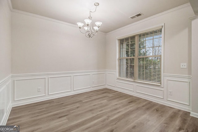 empty room featuring hardwood / wood-style floors, crown molding, and an inviting chandelier