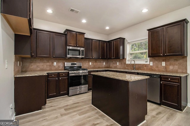 kitchen featuring sink, light stone countertops, a kitchen island, dark brown cabinetry, and stainless steel appliances