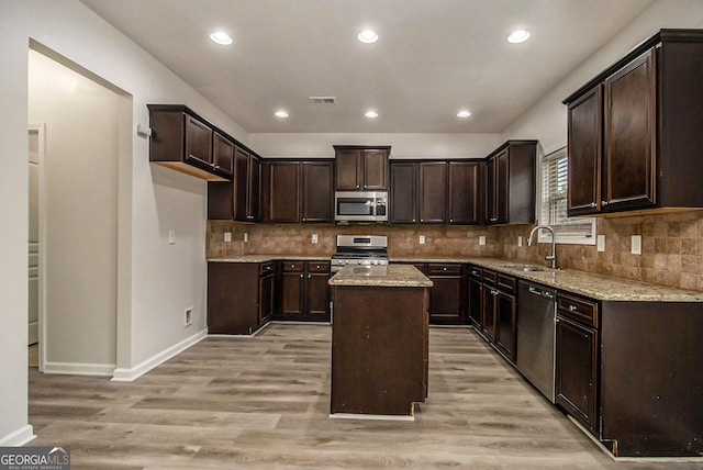 kitchen with a center island, sink, stainless steel appliances, light stone counters, and light hardwood / wood-style flooring