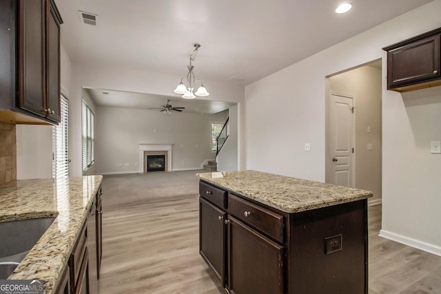 kitchen featuring light stone countertops, a center island, light hardwood / wood-style floors, decorative light fixtures, and ceiling fan with notable chandelier