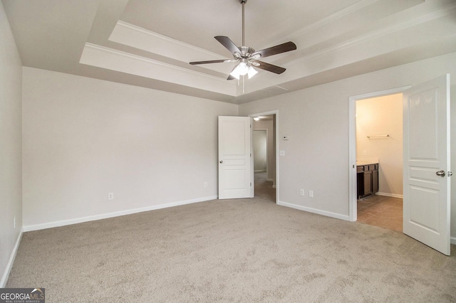 unfurnished bedroom featuring a tray ceiling, ensuite bath, ceiling fan, and light colored carpet