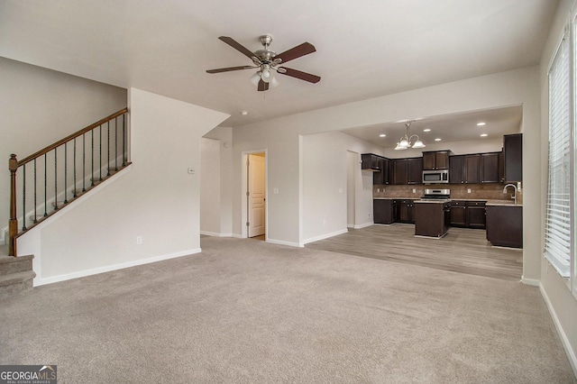 unfurnished living room featuring light carpet, ceiling fan with notable chandelier, and sink