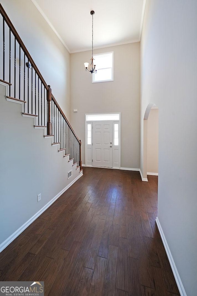 entryway with a notable chandelier, a high ceiling, ornamental molding, and dark wood-type flooring