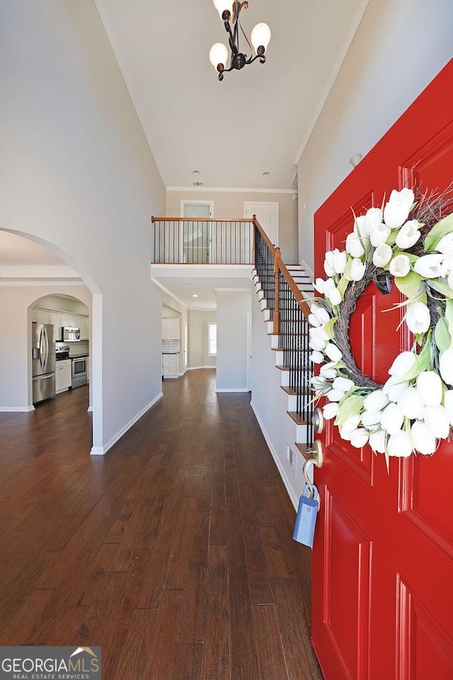 foyer entrance with crown molding, dark wood-type flooring, a high ceiling, and an inviting chandelier