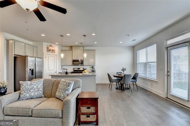 living room featuring ceiling fan, sink, and light wood-type flooring