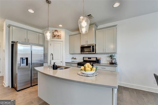 kitchen with gray cabinetry, an island with sink, stainless steel appliances, and decorative light fixtures